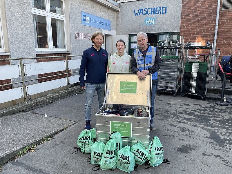 Two employees from SCC EVENTS and one employee from the City Mission are standing behind the donated products, smiling into the camera.