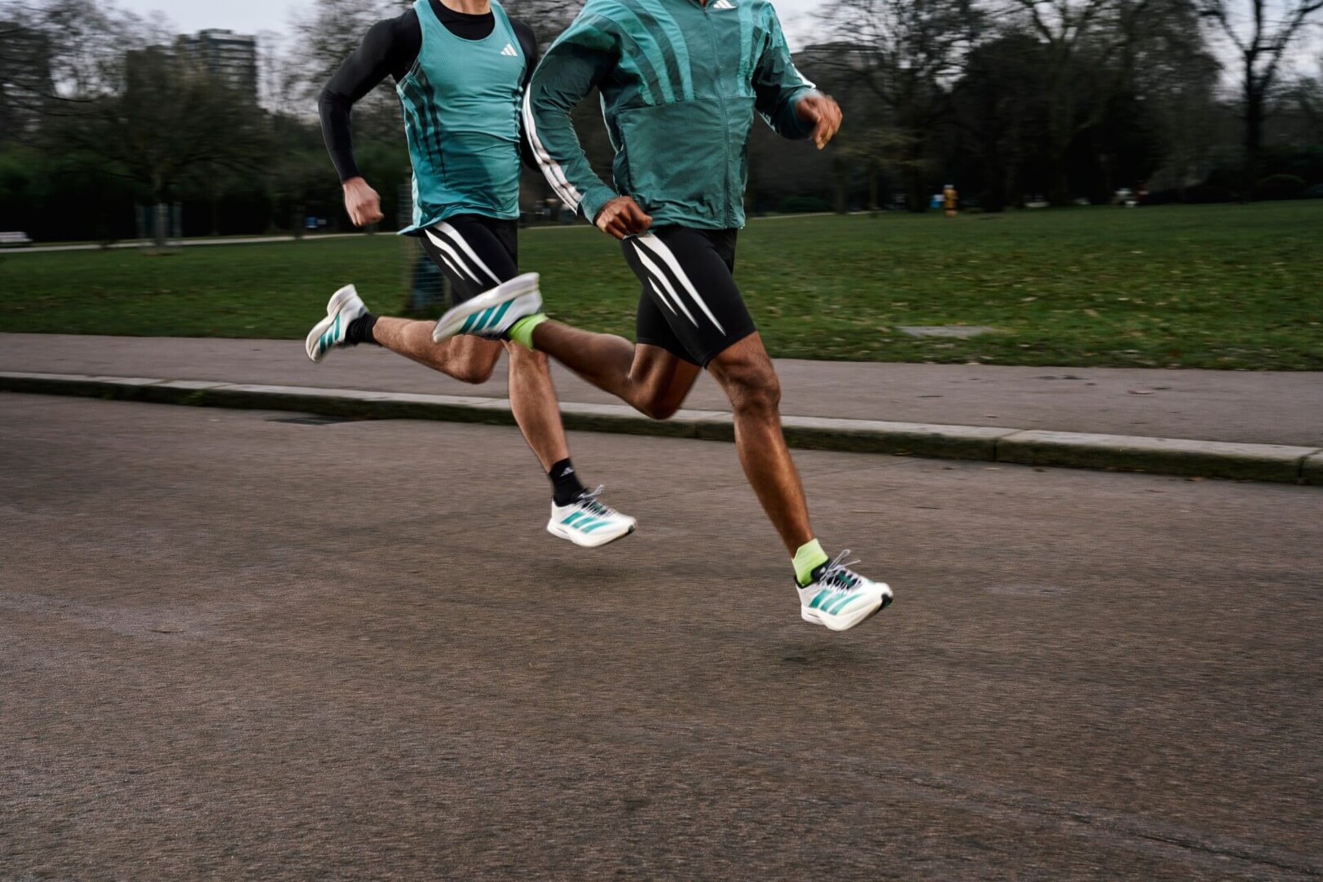 Two runners in black, white, and green adidas outfits jogging. Legs and the upper body are visible.