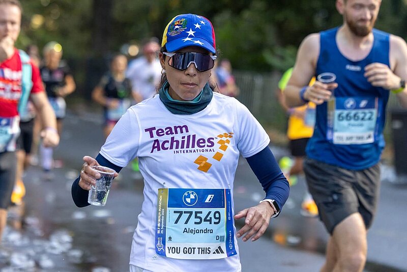 Läuferin beim BERLIN-MARATHON mit Wasserbecher in der Hand, Kopfbedeckung und Sonnenbrille.