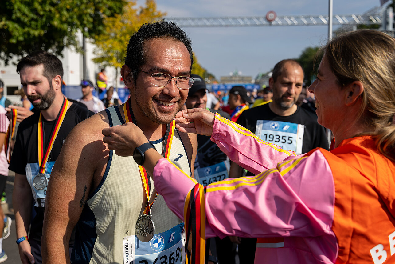 BMW BERLIN-MARATHON Finisher bekommt seine Medaille. Glücklicher Finisher des BMW BERLIN-MARATHON bekommt von einem Volunteer die Medaille um den Hals gehängt. ©Tilo Wiedensohler / SCC EVENTS