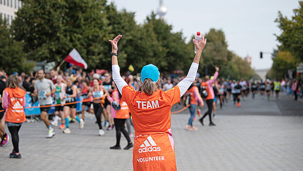 Ein Volunteer als Streckenposten hebt beide Hände, um die Läufer:innen vor dem  Brandenburger in die richtige Richtung zu lenken  ©Annegret Hilse / SCC EVENTS