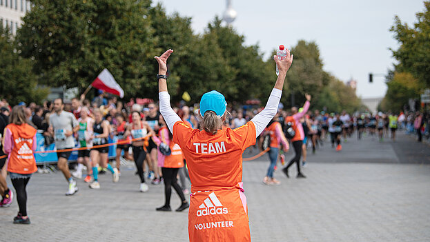 Ein Volunteer als Streckenposten hebt beide Hände, um die Läufer:innen vor dem Brandenburger in die richtige Richtung zu lenken ©Annegret Hilse / SCC EVENTS