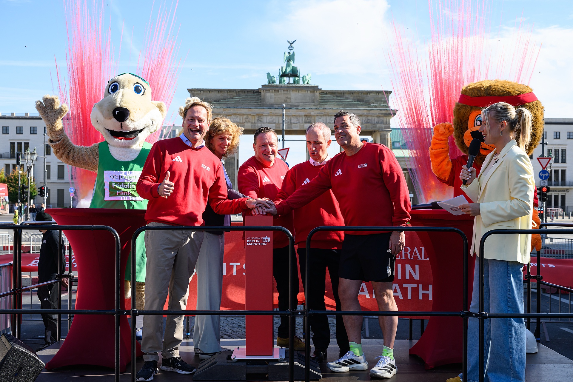 The SCC Events management team, dressed in red in front of the Brandenburg Gate, cheerfully presses the button together—all five of them—to launch registration for the 2027 GENERALI BERLIN Marathon.