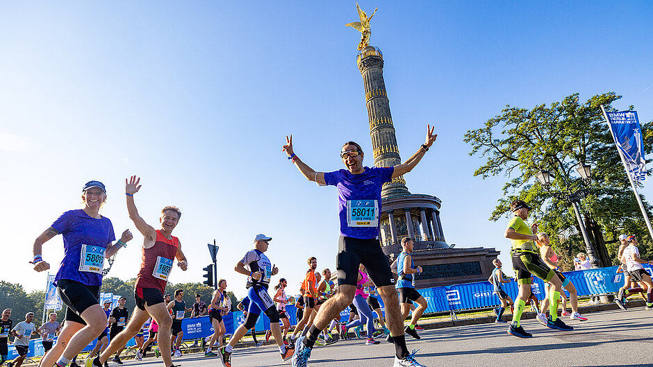 Participants run past the Victory Column and long advertising banners Happy waving participants run past the Victory Column carrying bibs with advertising logos. Behind them you can see a long advertising banner and flags waving in the wind.