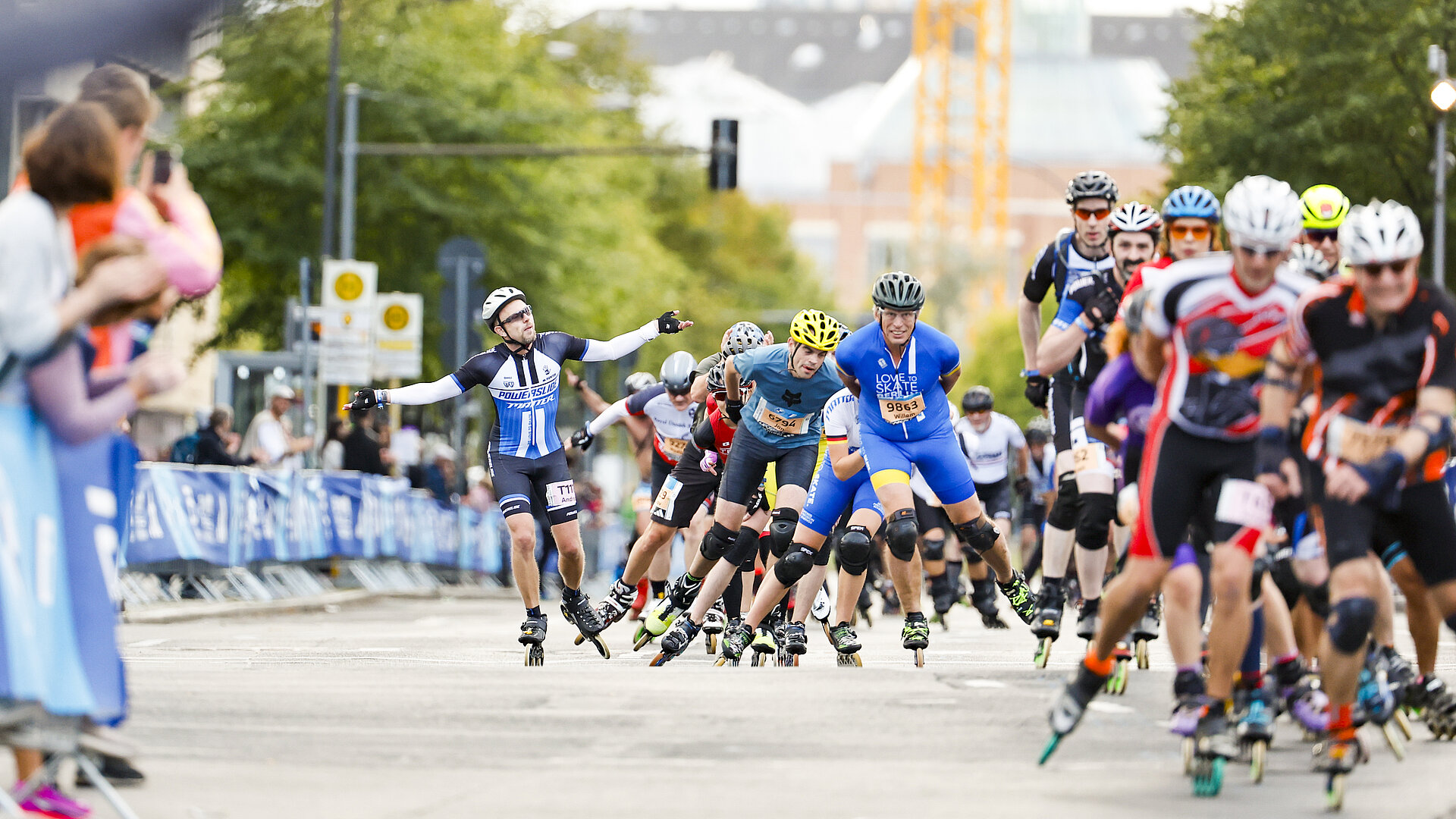 Inline skaters on the track. One of the skaters cheers on the crowd with his arms raised.