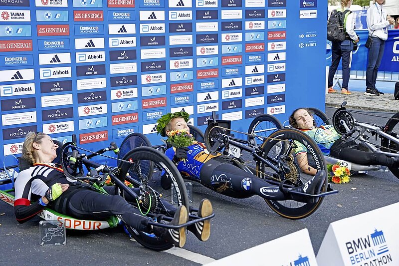 The 2023 handbike winners on the podium in their bikes. Julia Dierkesman with a laurel wreath on her head.