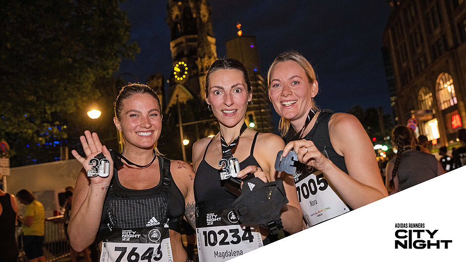 Finisherinnen präsentieren die Medaille der adidas Runners City Night.   Stolze und glückliche Finisherinnen der adidas Runners City Night präsentieren ihre Medaillen mit der Gedächtnis-Kirche im Hintergrund. ©Tilo Wiedensohler / SCC EVENTS