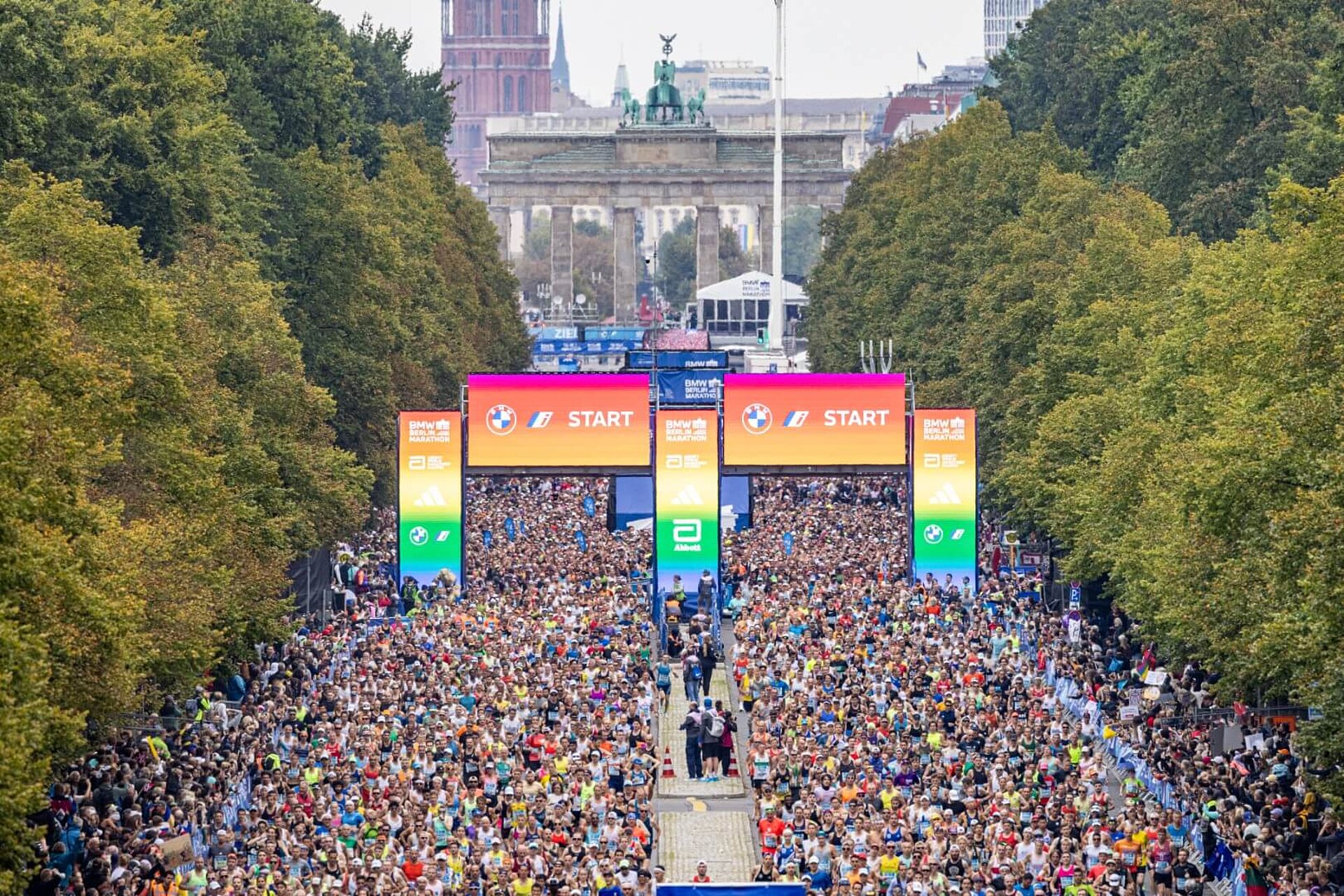 Masse an Läufer:innen durchquert das Starttor, das in Regenbogenfarben leuchtet.