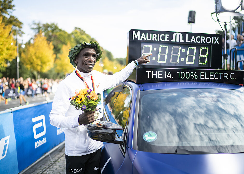 Kipchoge zeigt auf Weltrekordzeit Eliod Kipchoge zeigt auf eine Uhr, auf der sein Weltrekord zu sehen ist.