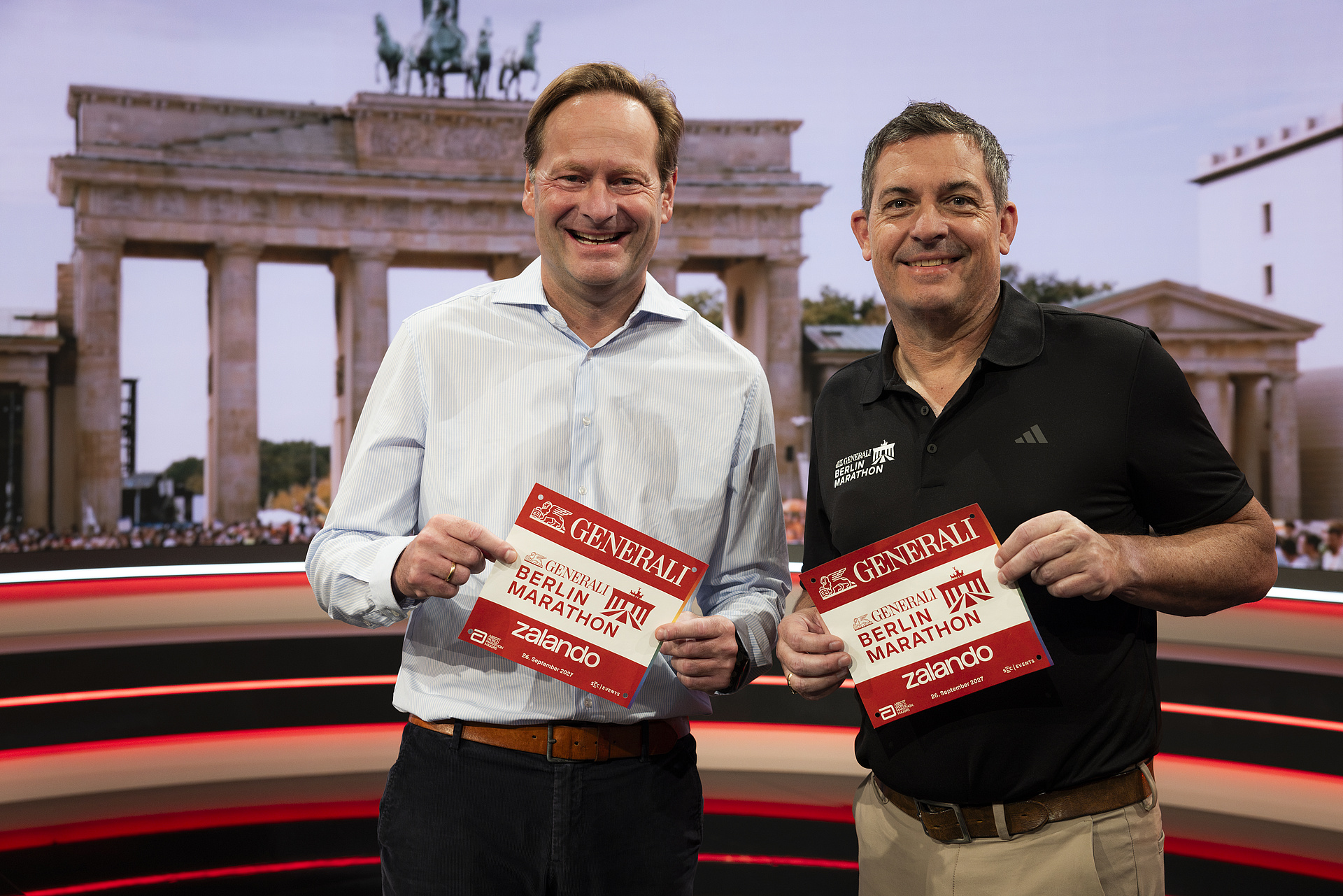 The two CEOs smile as they hold up a race number featuring the Generali Berlin Marathon logo for the camera.